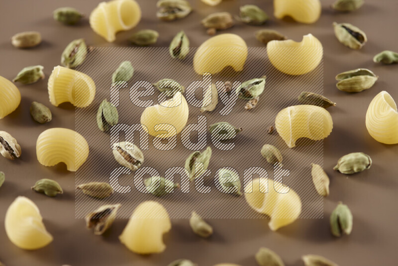 Raw pasta with different ingredients such as cherry tomatoes, garlic, onions, red chilis, black pepper, white pepper, bay laurel leaves, rosemary and cardamom on beige background