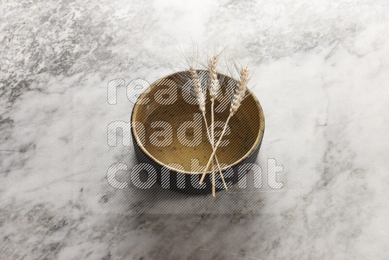 Wheat stalks on multicolored pottery oven plate on grey marble background