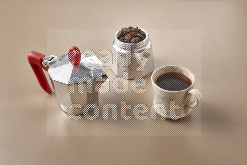 A moka pot with red handle surrounded by roasted coffee beans on beige background