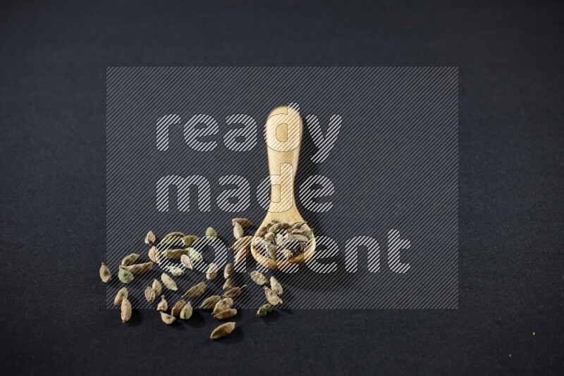 A wooden spoon full of cardamom on black flooring