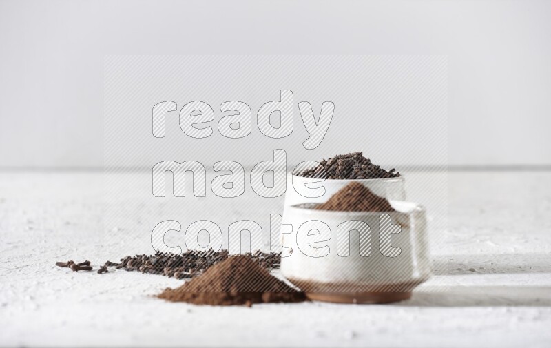 2 Beige ceramic bowls, one full of cloves and the other full of powder on textured white flooring