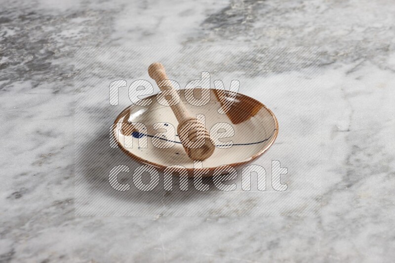 Multicolored pottery plate with wooden honey dipper in it on grey marble background