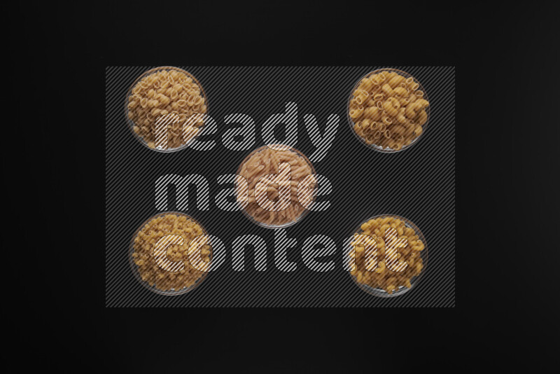 Different pasta types in 5 glass bowls on black background