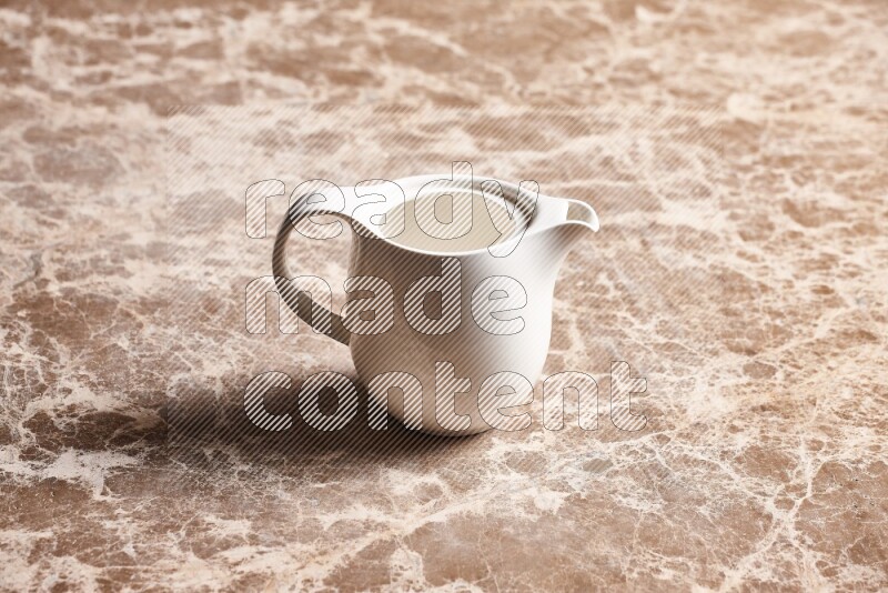 A ceramic milk jug on beige marble background