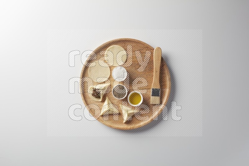 two closed sambosas and one open sambosa filled with meat while salt, black pepper and oil with oil brush aside in a wooden dish on a white background