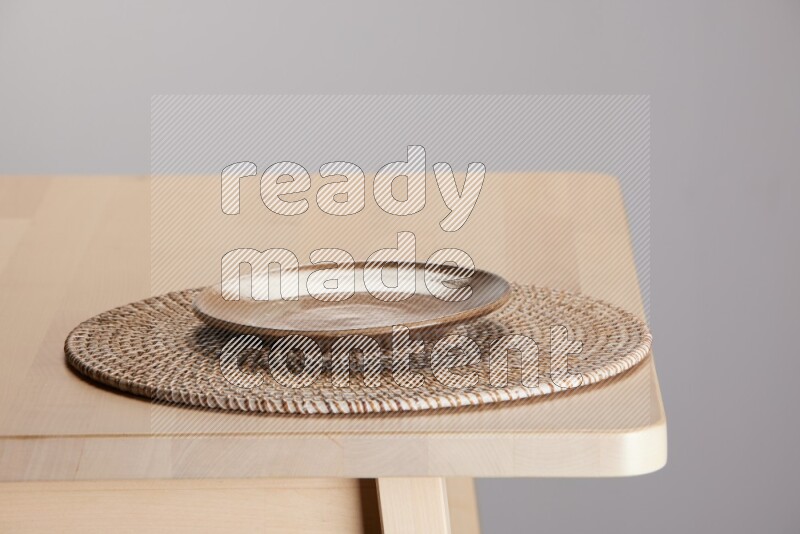 multi-colored pottery Plate placed on a big light colored straw placemat on the edge of wooden table