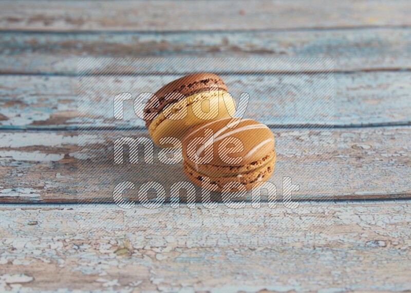 45º Shot of of two assorted Brown Irish Cream, and Yellow, and Brown Chai Latte macarons  on light blue background