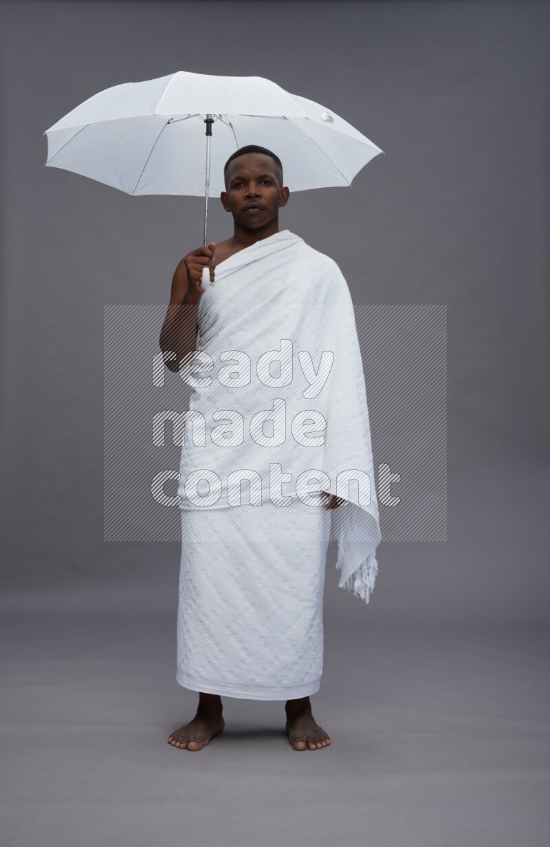 A man wearing Ehram Standing holding umbrella on gray background