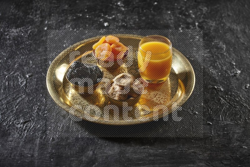 Dried fruits in metal bowls with qamar eldin on a tray in dark setup
