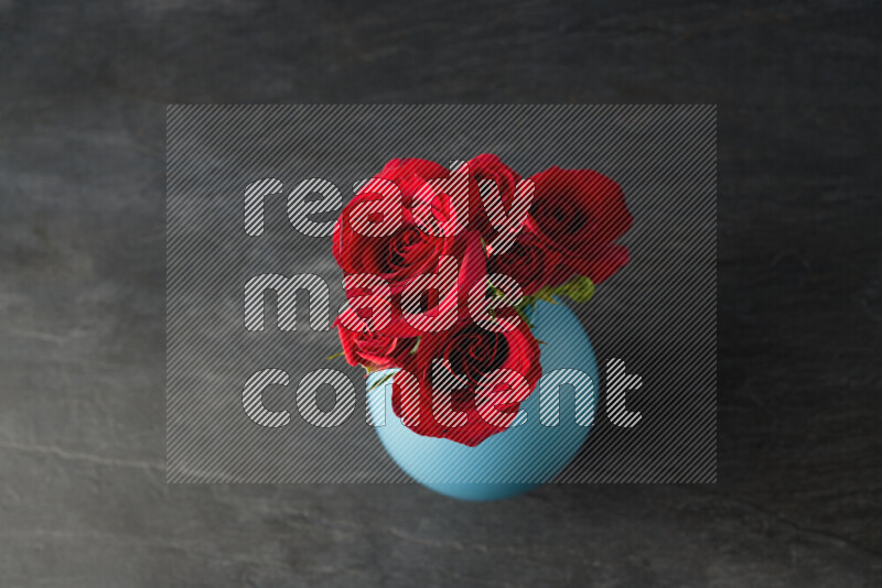 An arrangement of vivid red roses in a blue vase on black marble background