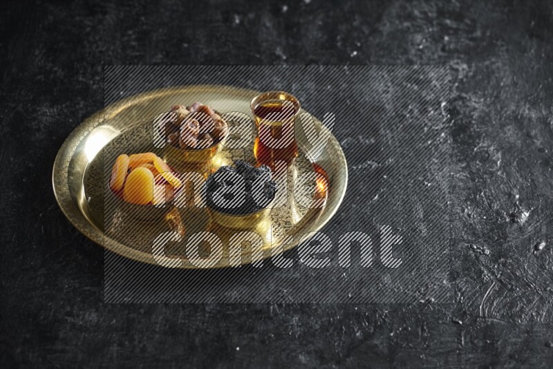 Dried fruits in metal bowls on a tray in a dark setup