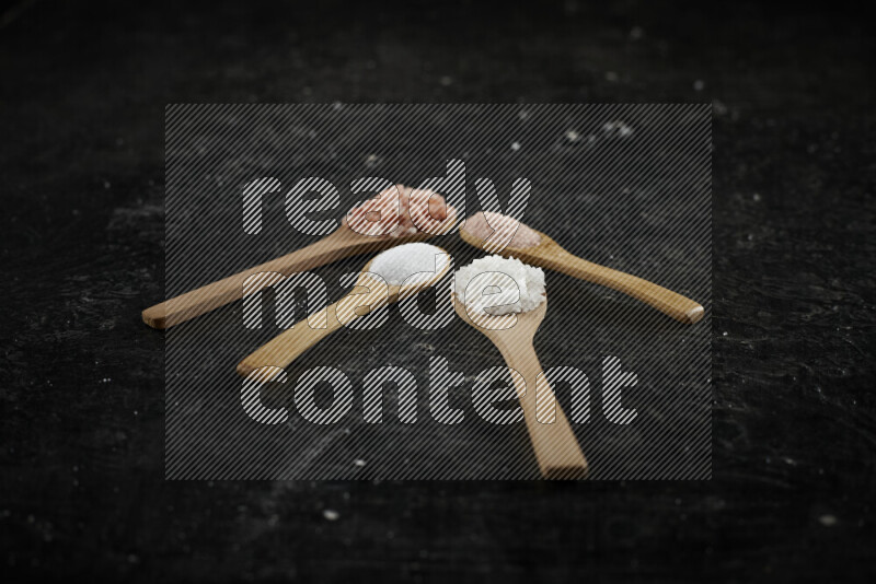4 wooden spoons filled with fine and coarse salt on black background