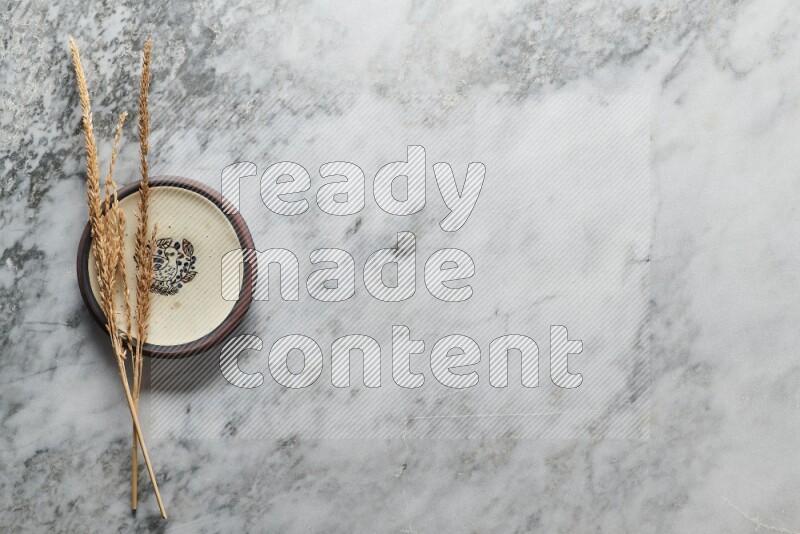 Wheat stalks on decorative pottery plate on grey marble background