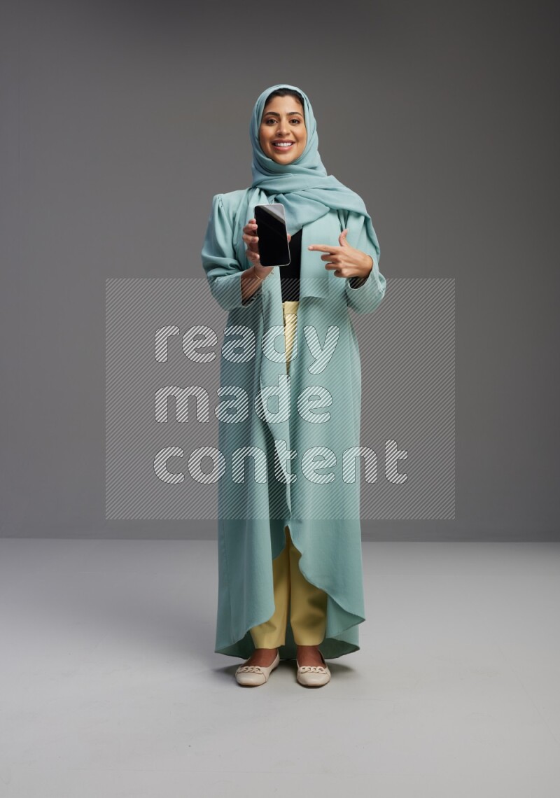Saudi Woman wearing Abaya standing showing phone to camera on Gray background