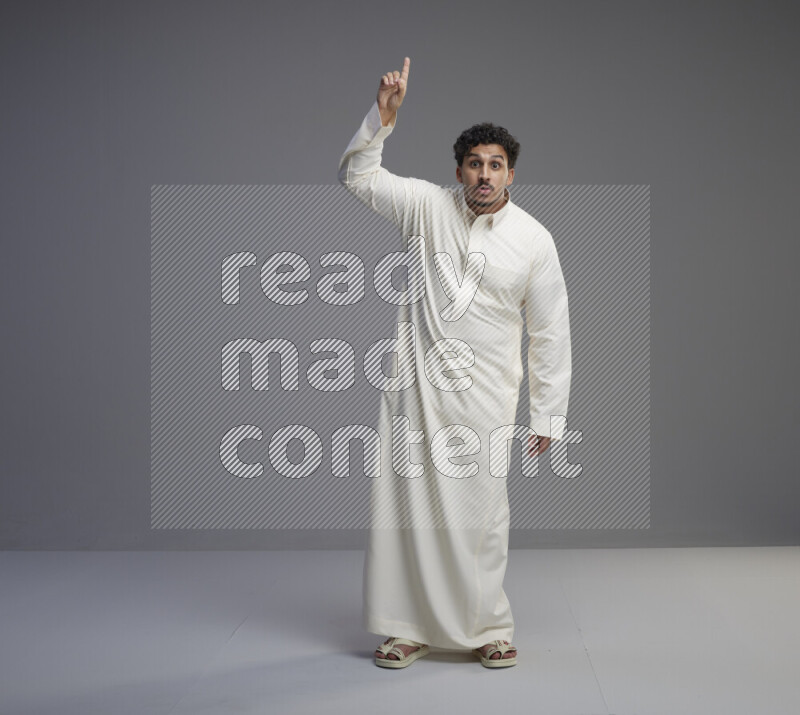 A Saudi man standing wearing thob interacting with the camera on gray background