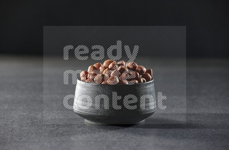 A black pottery bowl full of peeled hazelnuts on a black background in different angles