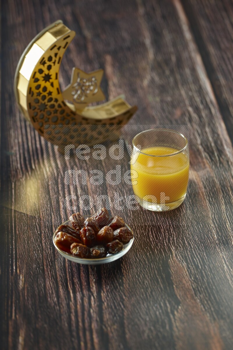 A wooden golden crescent lantern with different drinks, dates, nuts, prayer beads and quran on brown wooden background