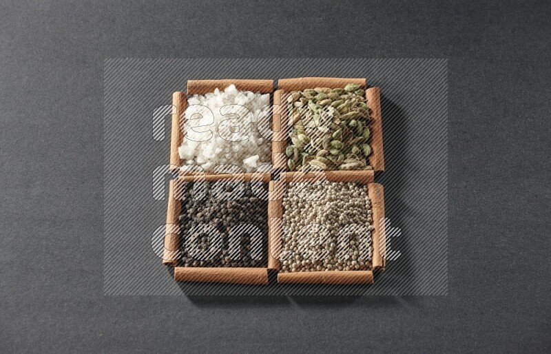 4 مربعات من عيدان القرفة ممتلئة بحبوب الفلفل الأسود والفلفل الأبيض وحب الهيل والملح الأبيض على أرضية سوداء