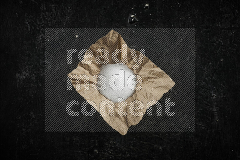 A crumpled piece of paper full of white salt on black background