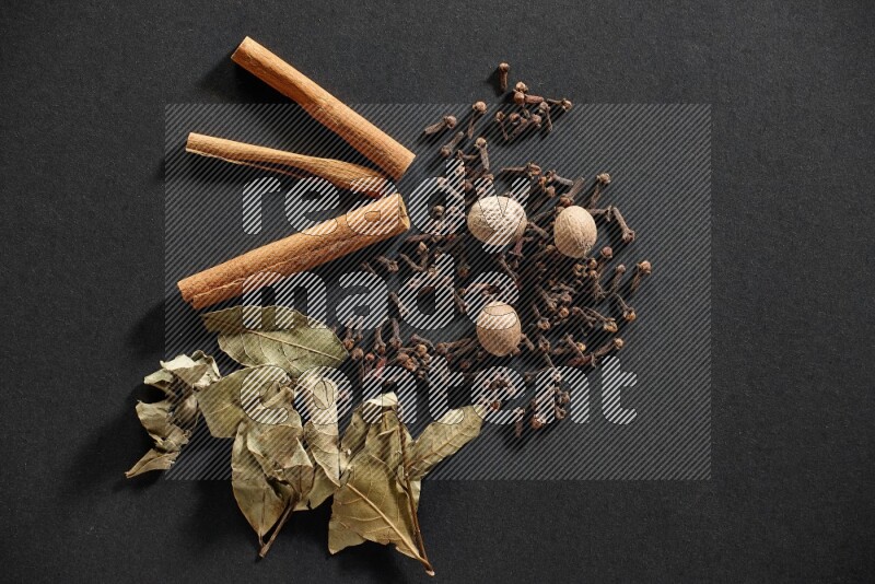 Cloves, ginger, bay laurel and cinnamon sticks on black flooring