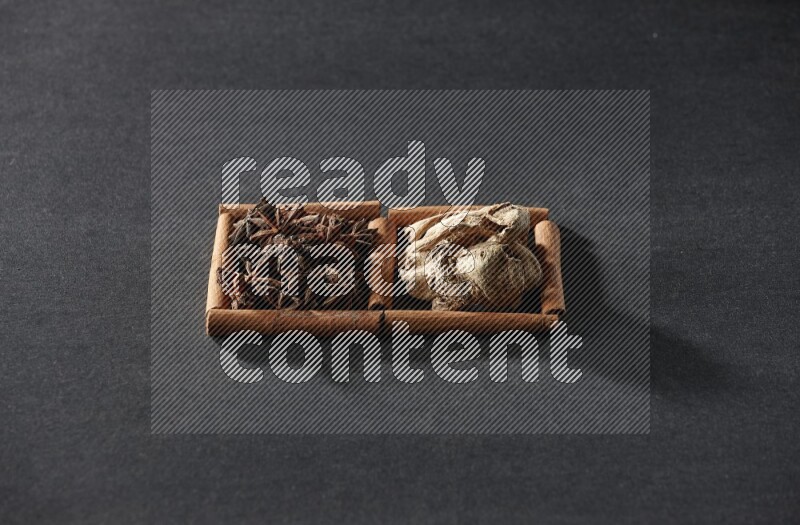 مربعان من أعواد القرفة ممتلئان باليانسون النجمي والزنجبيل المجفف علي خلفية سوداء