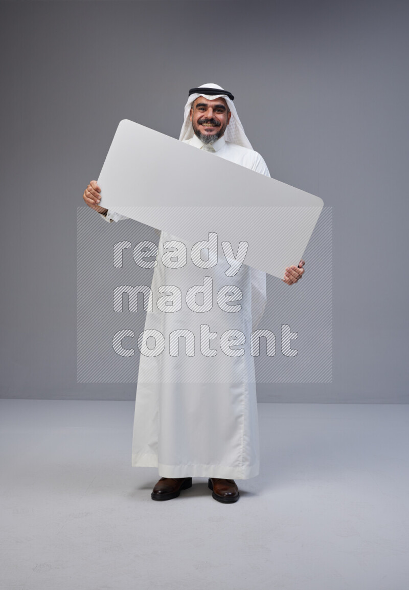 Saudi man Wearing Thob and white Shomag standing holding board on Gray background