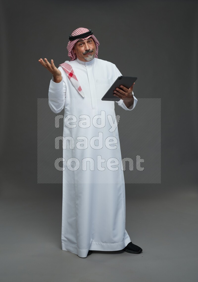 Saudi man with shomag Standing working on tablet on gray background
