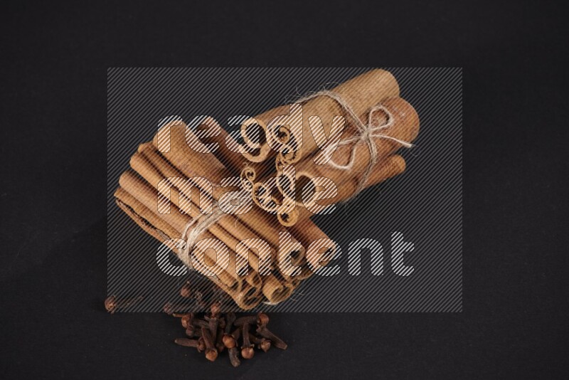 Two bounded stacks of cinnamon sticks with cloves on black background