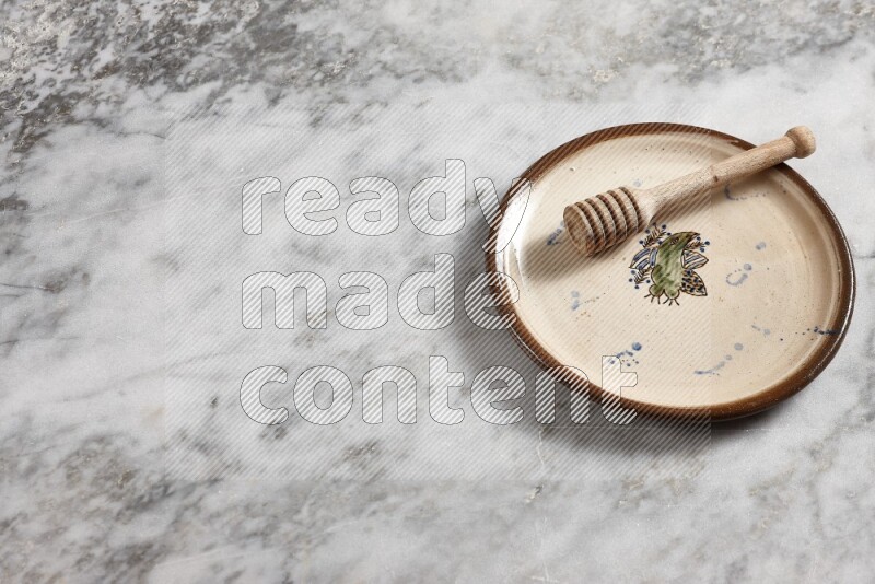 Decorative pottery plate with wooden honey dipper in it on grey marble background
