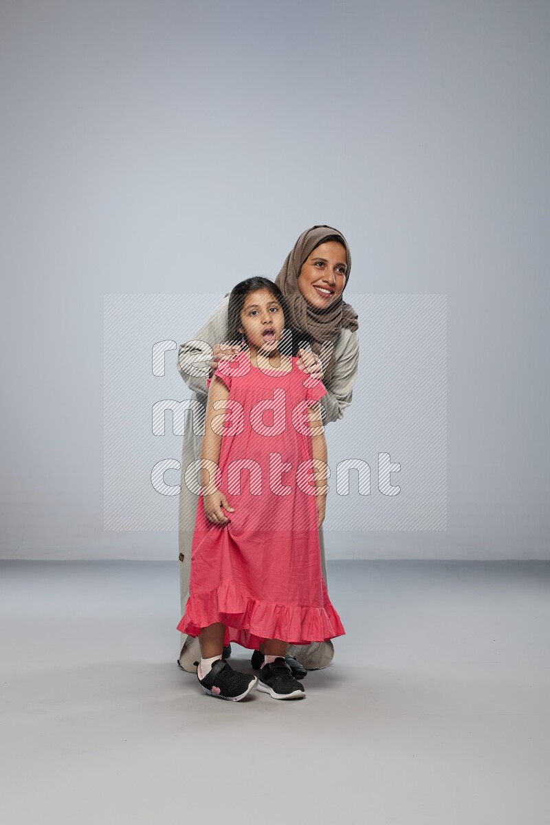 A girl and her mother interacting with the camera on gray background