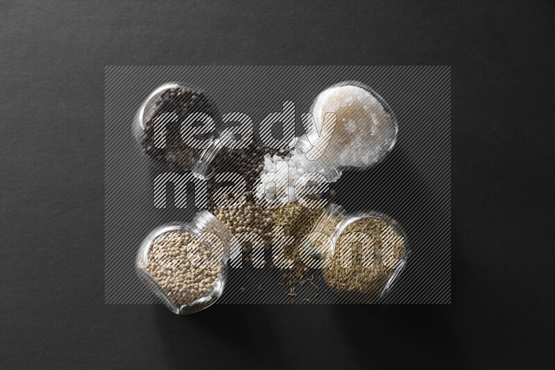 4 glass spice jars full of salt, black peppers, white peppers and cumin on black flooring