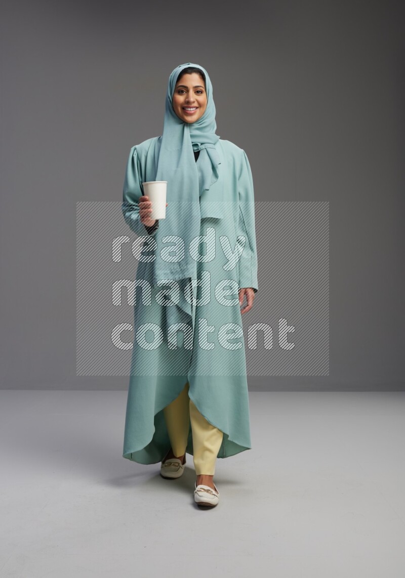 Saudi Woman wearing Abaya standing  holding paper cup on Gray background
