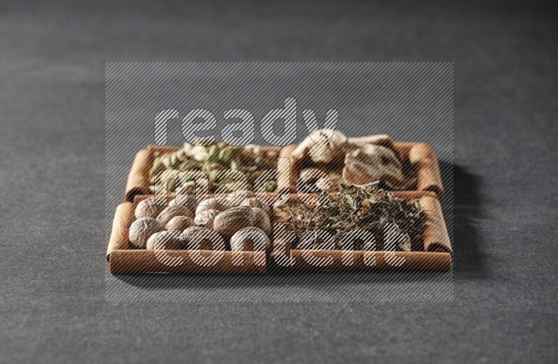 4 مربعات من عيدان القرفة ممتلئة بالريحان المجفف والهيل والزنجبيل المجفف وجوزة الطيب على أرضية سوداء