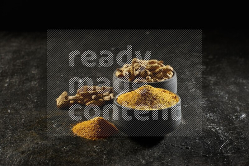 وعاءان من الفخار باللون الأسود، أحدهما ممتلئ ببودرة الكركم والآخر ممتلئ بأصابع كاملة من الكركم المجفف على خلفية سوداء