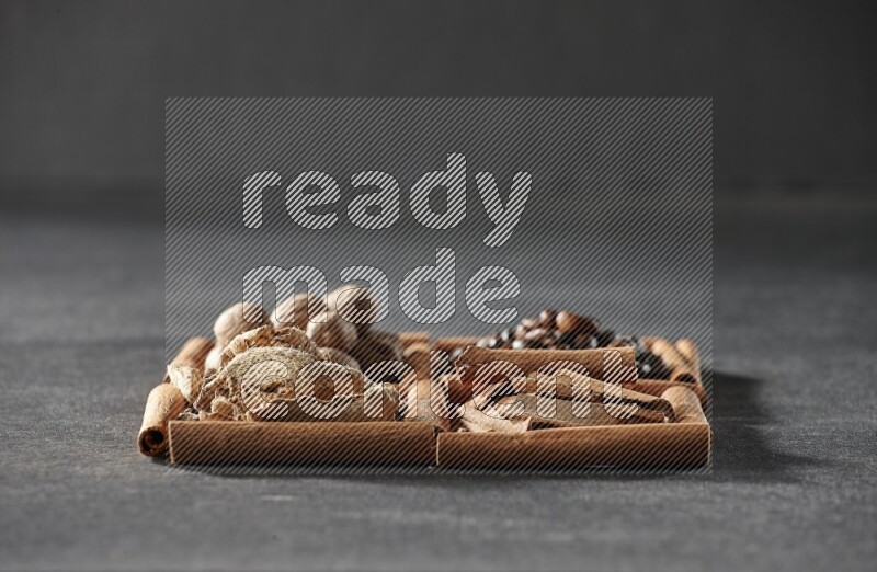 4 مربعات من عيدان القرفة ممتلئة بحبوب القهوة وقطع القرفة والزجبيل المجفف وجوزة الطيب على أرضية سوداء