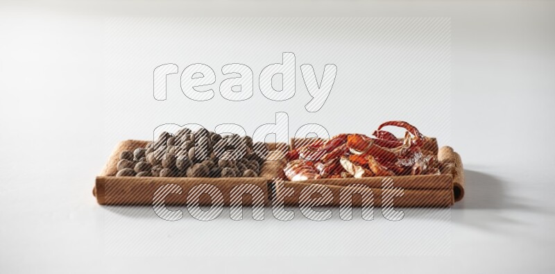 مربعان من أعواد القرفة ممتلئان بالفلفل الحار المجفف وحبوب بهار الفلفل الحلو علي خلفية بيضاء