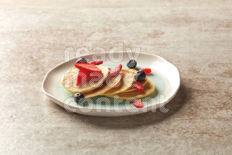 Five stacked mixed berries mini pancakes in a bicolor plate on beige background