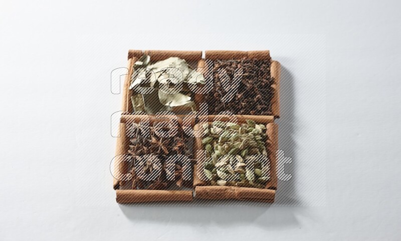 4 مربعات من أعواد القرفة ممتلئة بالهيل واليانسون والقرنفل وأوراق الغار على أرضية بيضاء