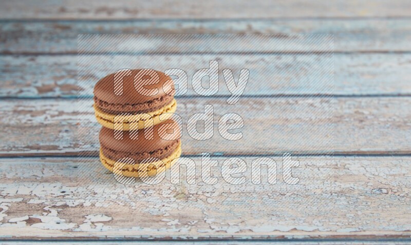 45º Shot of two Yellow and Brown Chai Latte macarons on light blue wooden background