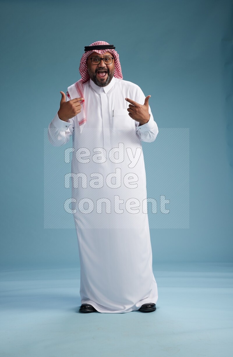 Saudi Man with shimag Standing Interacting with the camera on blue background