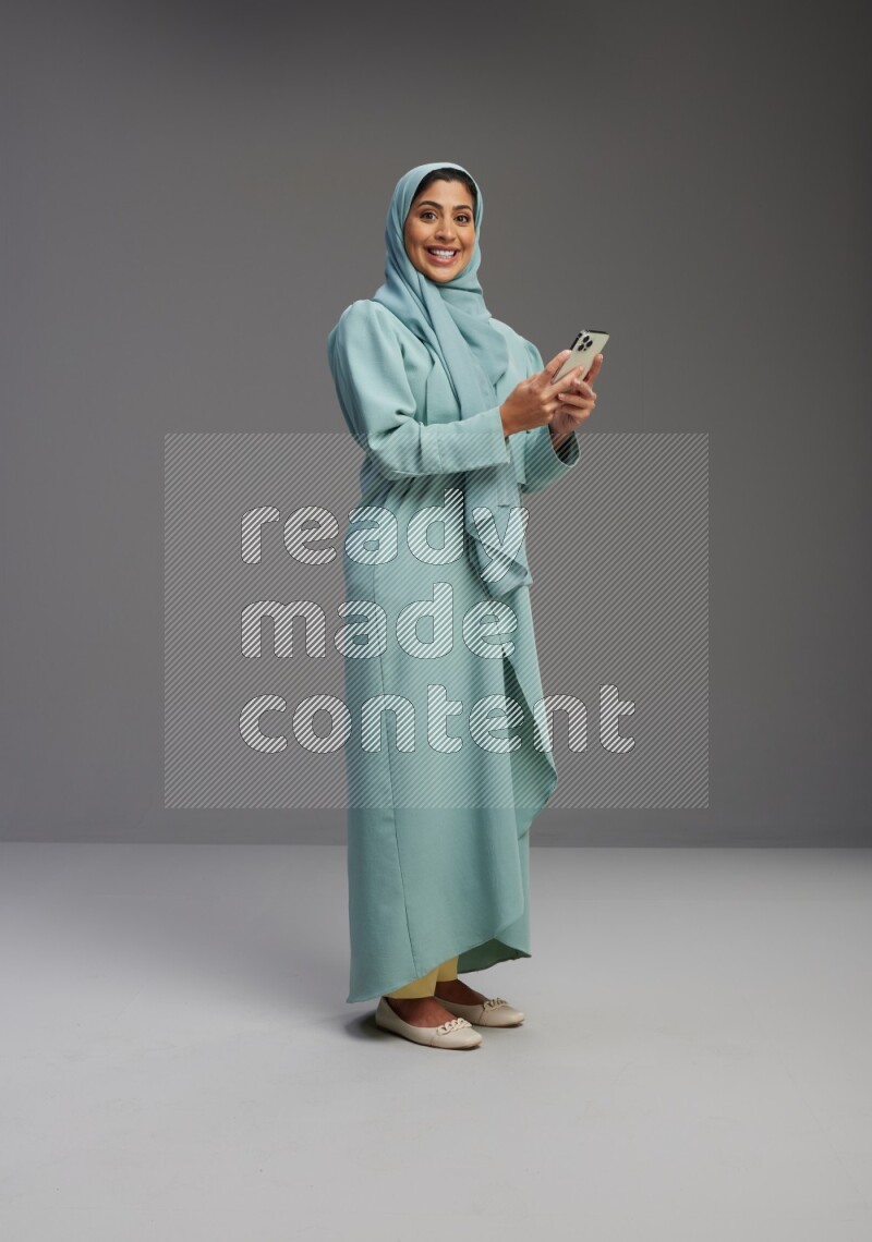 Saudi Woman wearing Abaya standing texting on phone on Gray background