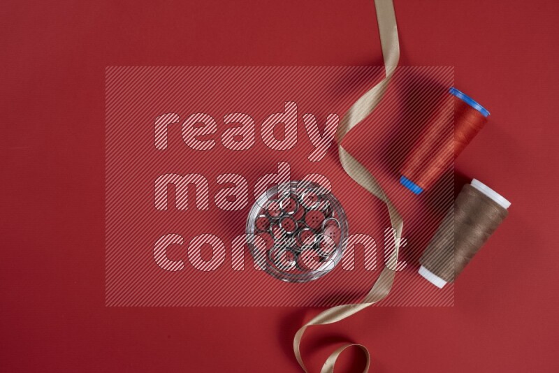 A brown and red collection of sewing and tailoring tools arranged on a red background