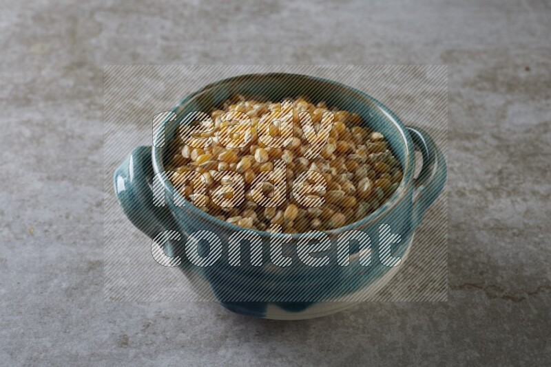 corn kernel in a multi-colored handheld ceramic bowl on a grey textured countertop