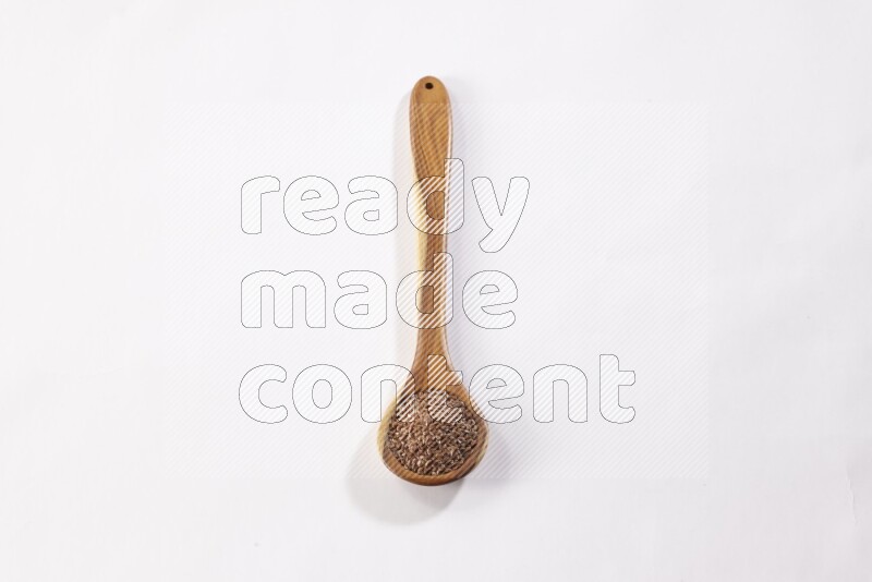 A wooden ladle full of flax seeds on a white flooring