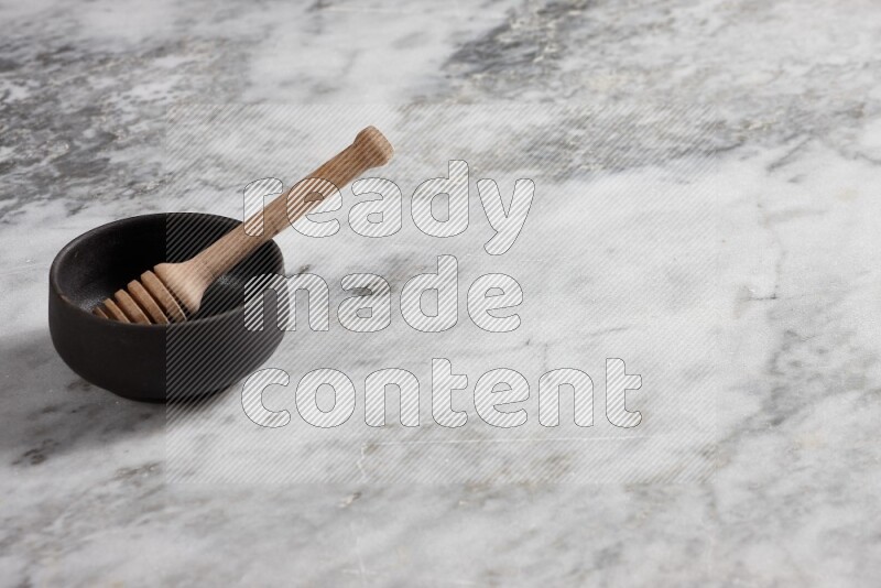 Black pottery bowl with wooden honey dipper in it on grey marble background