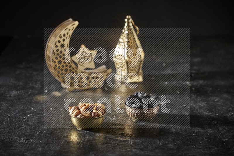 Nuts in a metal bowl with dried plums beside golden lanterns in a dark setup