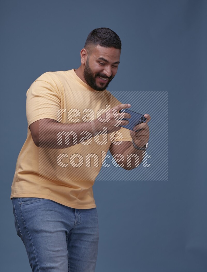 A man Playing Games on Smartphone on Blue Background wearing Orange T-shirt