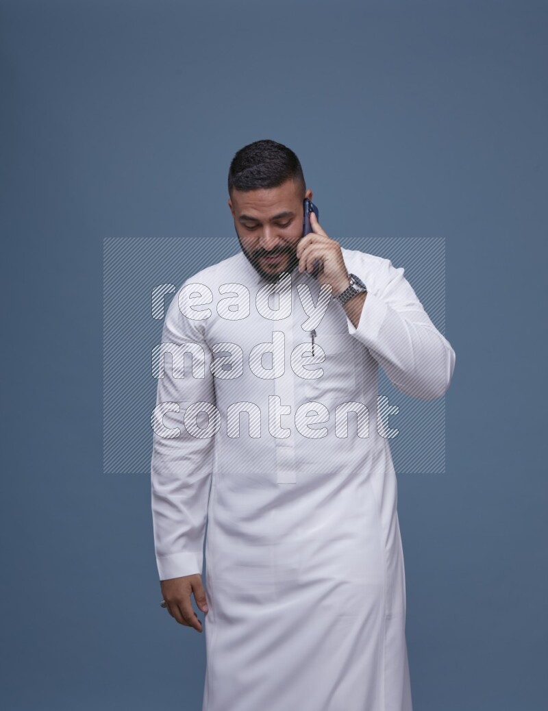 A Saudi man calling on blue background wearing Saudi Thob
