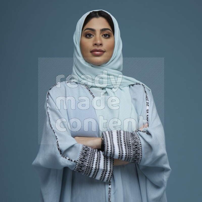 A woman posing in a blue background wearing a blue Abaya with hijab