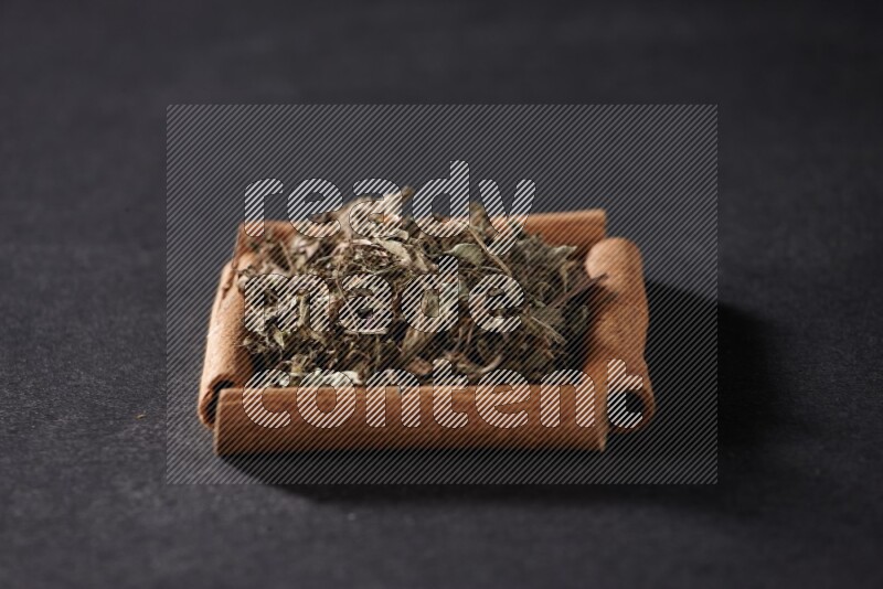 أربعة من أعواد القرفة مكونة شكل مربع بداخلها ريحان مجفف علي خلفية سوداء